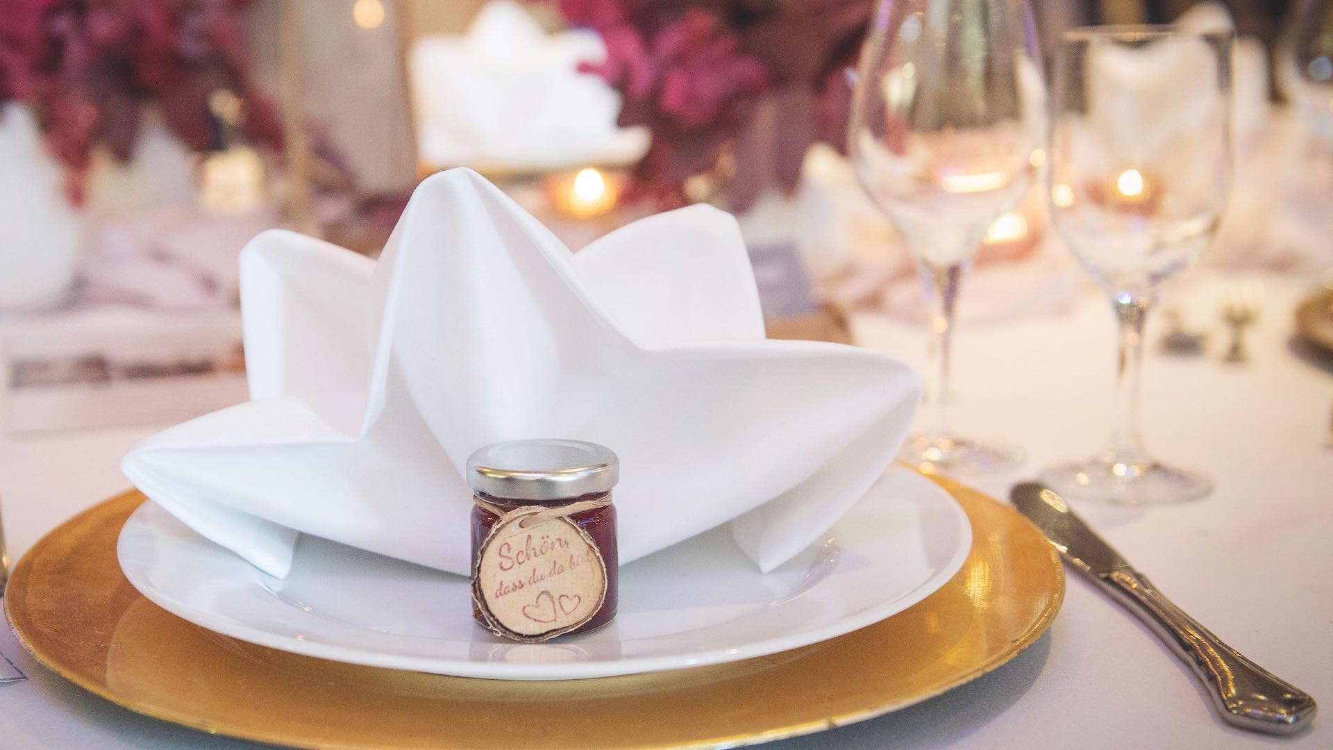 Gastgeschenk Hochzeit Heideblütenaufstrich mit Anhänger Schön dass du da bist dekoriert auf einem Tisch mit Gold und Dunkelrot